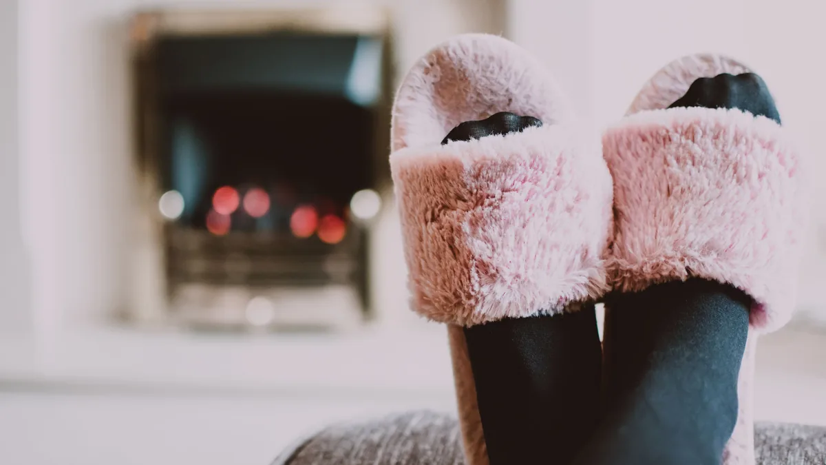 Füße in rosa Plüschpantoffeln, hochgelegt vor einem brennenden Kamin