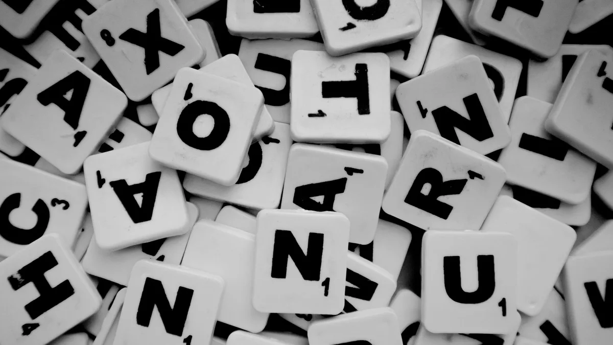Ein Haufen weißer Spielsteine mit schwarzen Buchstaben und kleinen Punktzahlen, in Schwarzweiß