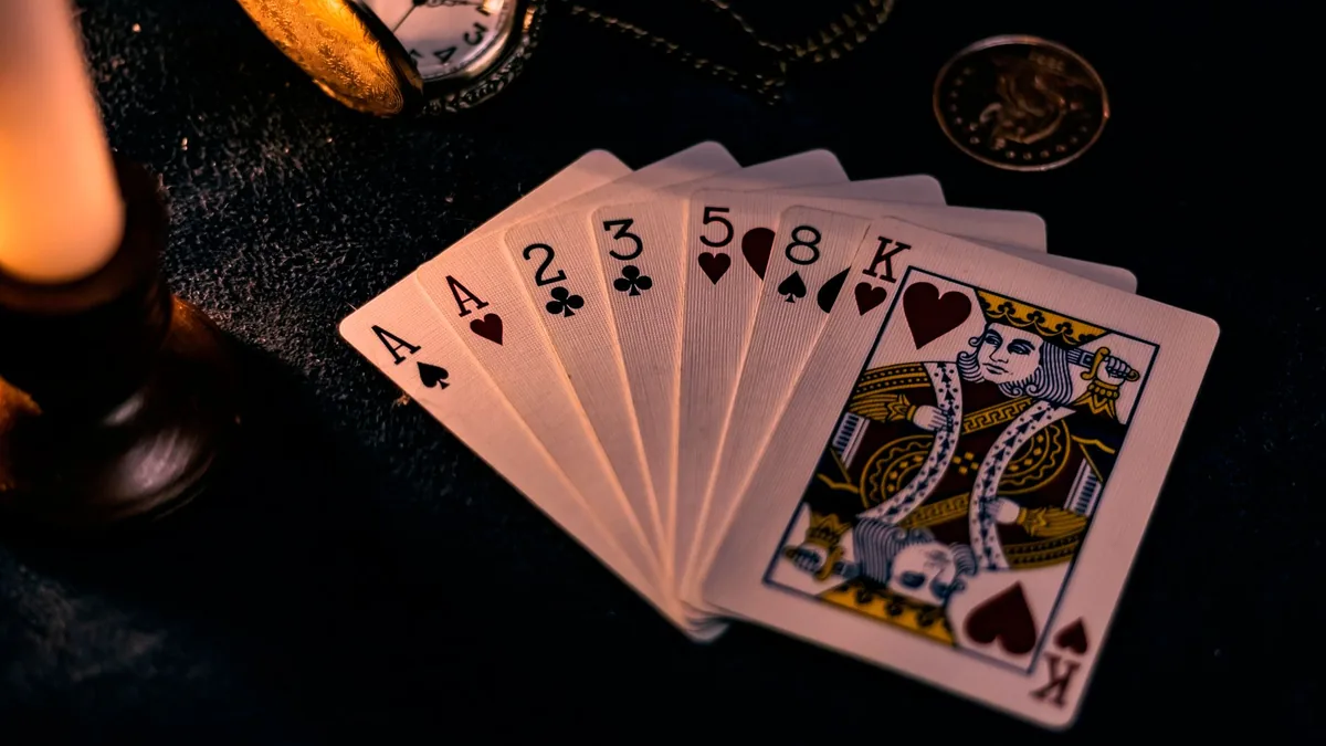 Aufgefächerte Spielkarten neben einer Kerze und einer Taschenuhr auf dunklem Grund