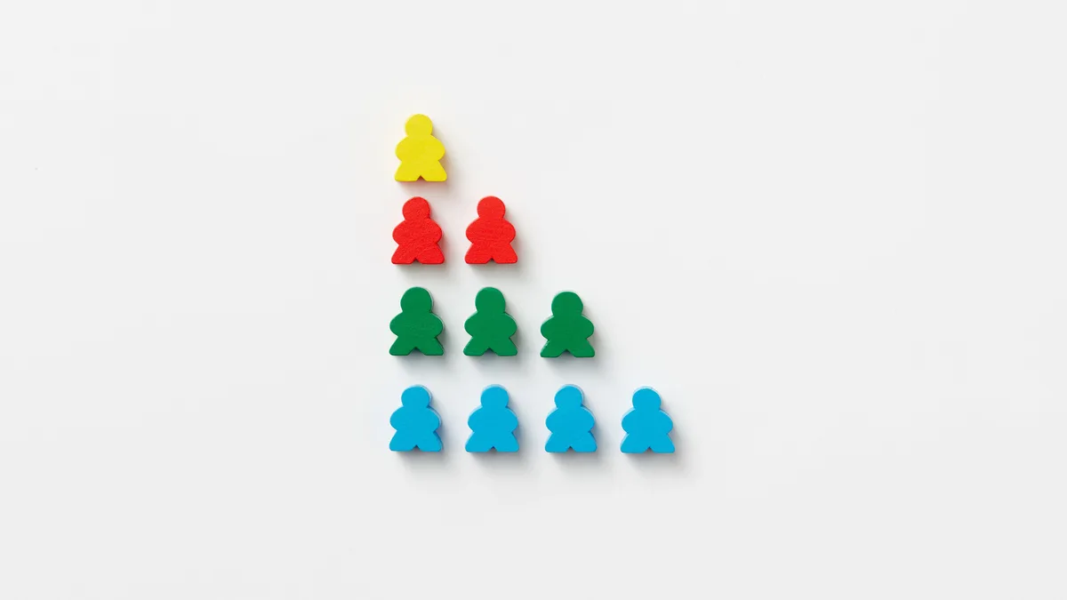 Zehn hölzerne Spielfiguren in Gelb, Rot, Grün und Blau, als vierstufige Treppe auf weißem Grund gelegt