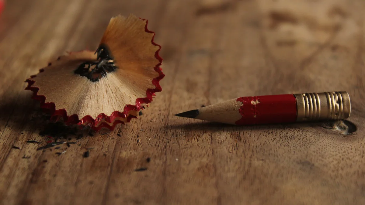Ein kurz gewordener roter Bleistift liegt neben einer Spanlocke auf einer Holzplatte