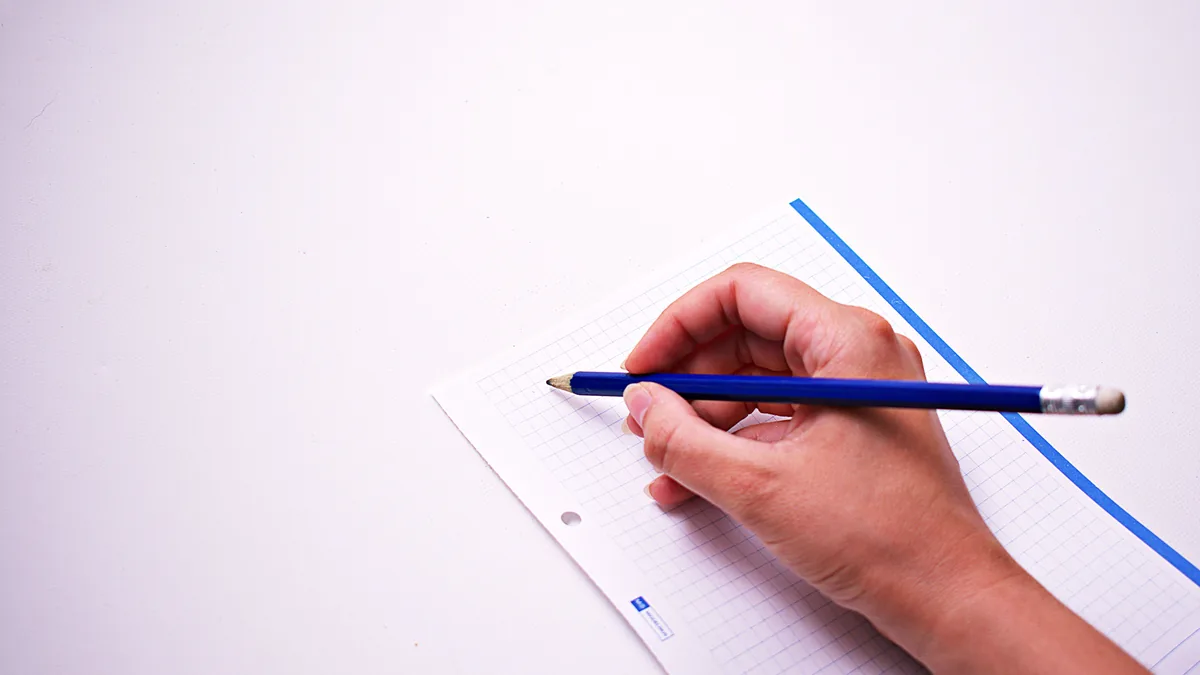 Eine Hand setzt einen blauen Bleistift auf ein leeres Blatt kariertes Papier