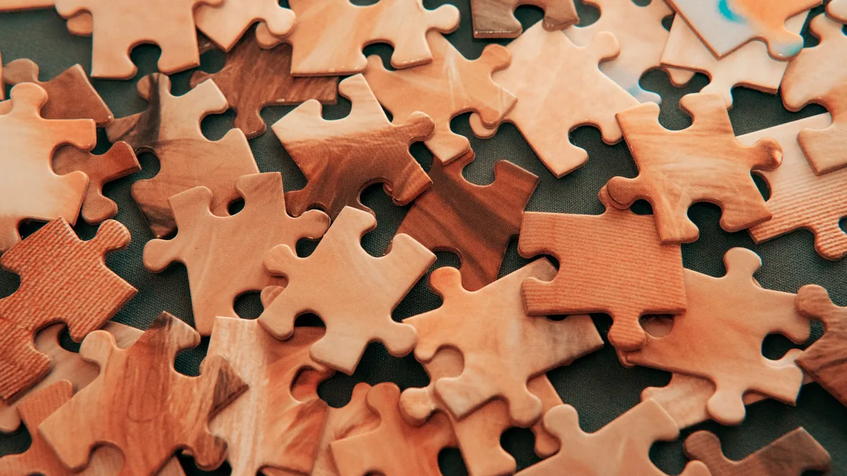 Verstreute Puzzleteile aus hellem Holz auf einer dunklen Fläche