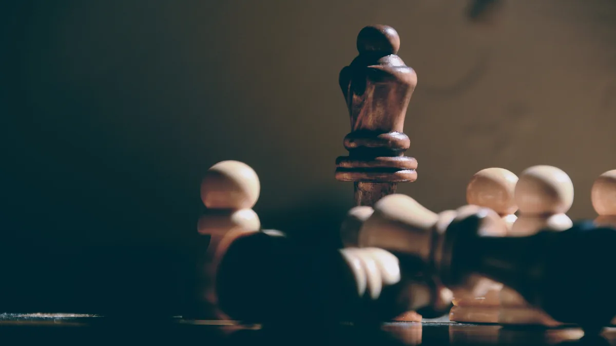 Eine dunkle Schachdame steht aufrecht, ringsum liegen umgefallene helle und dunkle Figuren