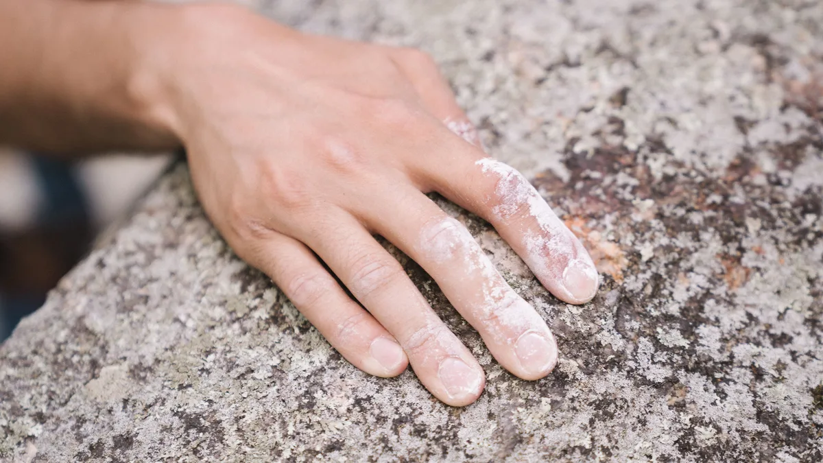 Eine Hand mit weißen Kreideresten an den Fingern liegt flach auf einem grauen, gesprenkelten Felsen