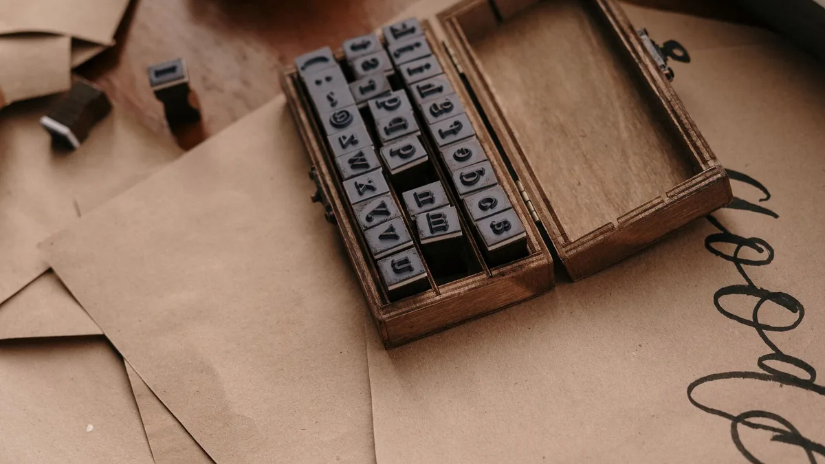 Ein offenes Holzkästchen mit Buchstabenstempeln liegt auf braunem Packpapier, daneben ein einzelner Stempel