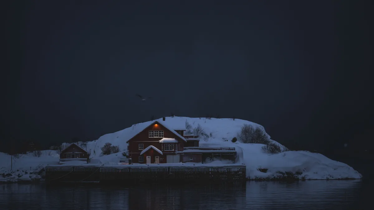 Ein einzeln stehendes Haus mit einem erleuchteten Fenster auf einer verschneiten Halbinsel bei Nacht
