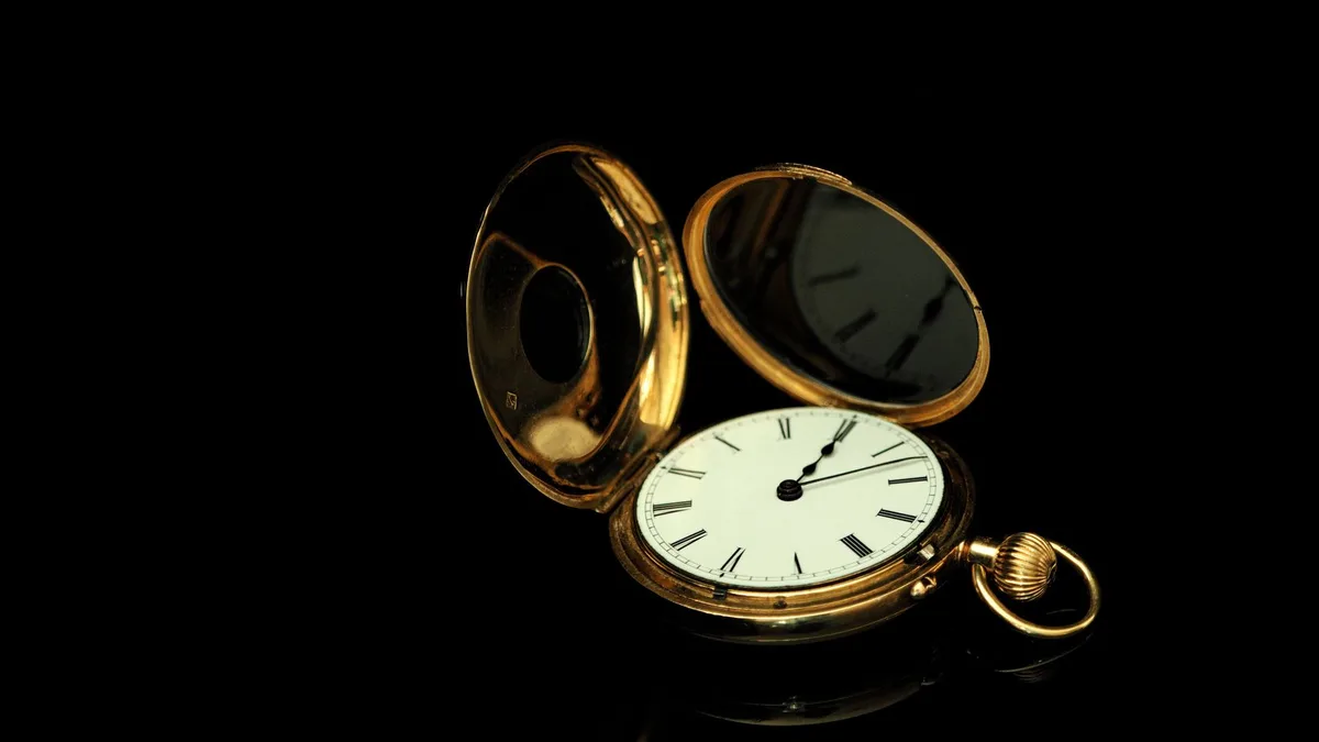 Eine aufgeklappte goldene Taschenuhr mit weißem Zifferblatt und römischen Ziffern vor schwarzem Hintergrund